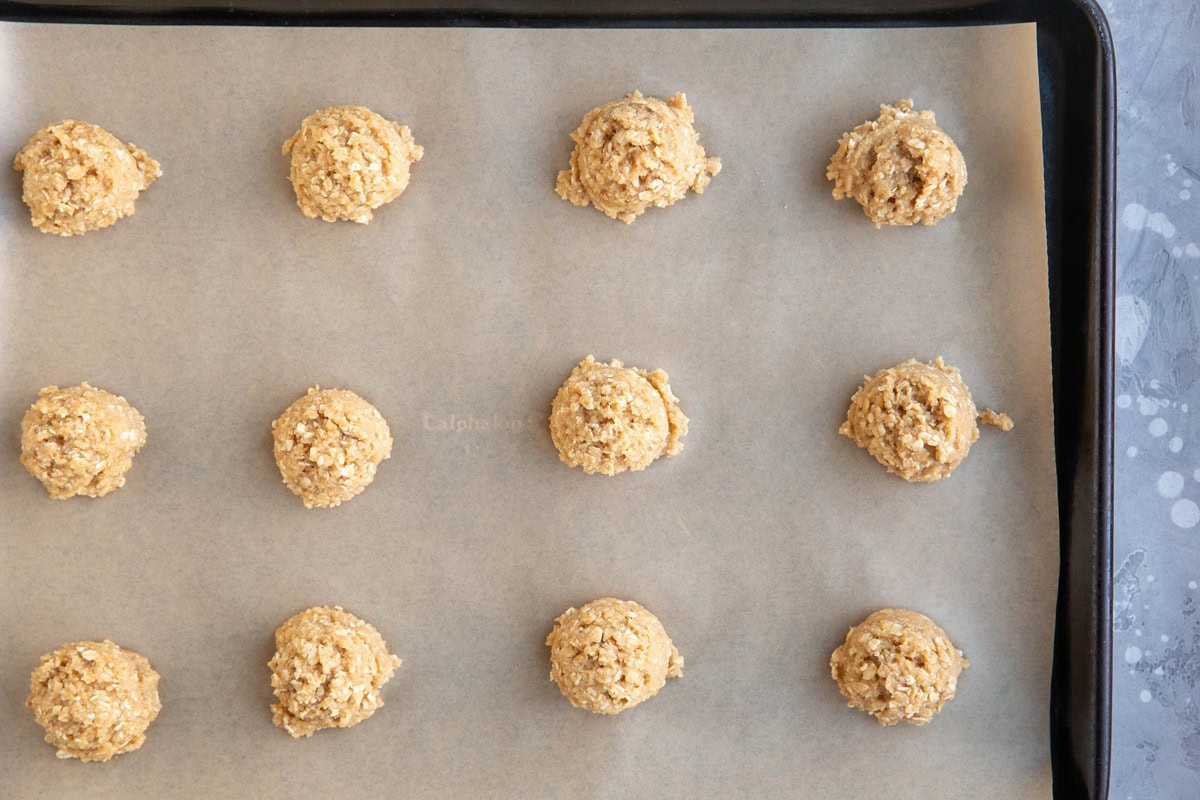 oatmeal cookie dough balls on a lined baking sheet to go into the oven to make cookies.