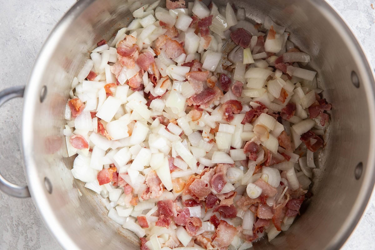 Stainless steel pot with onions and crispy bacon cooking.