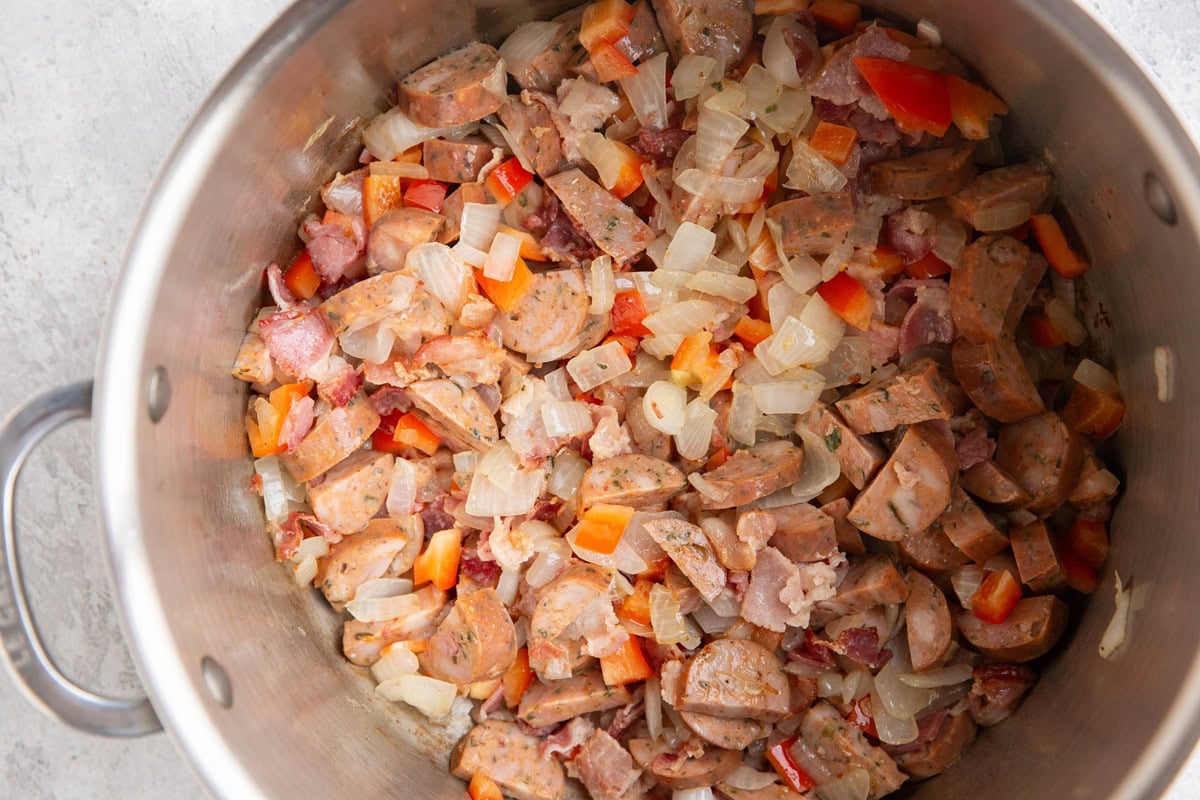 Large pot with onion, bell pepper, sausage, and bacon cooking.