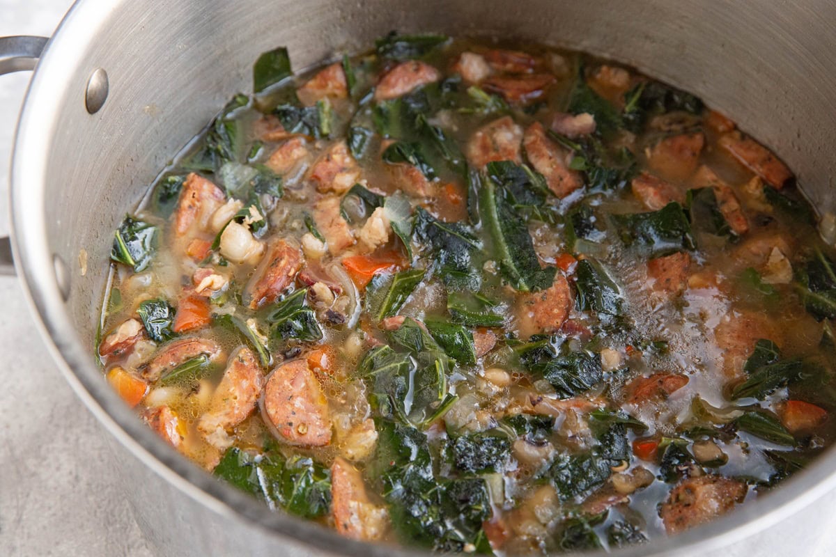large stainless steel pot of black eyed pea soup with collard greens, bacon, and sausage.