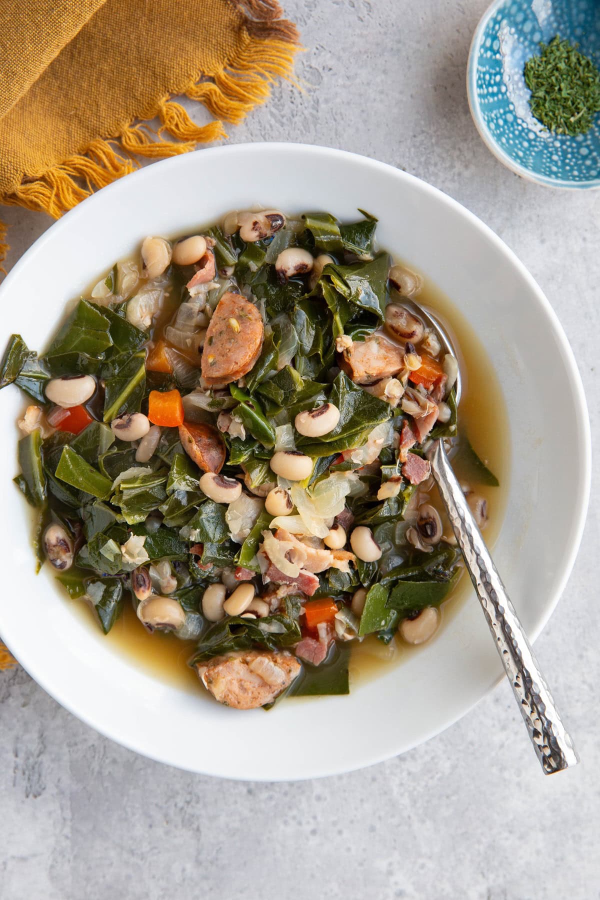 Large white bowl of black eyed pea soup with collard greens and sausage.