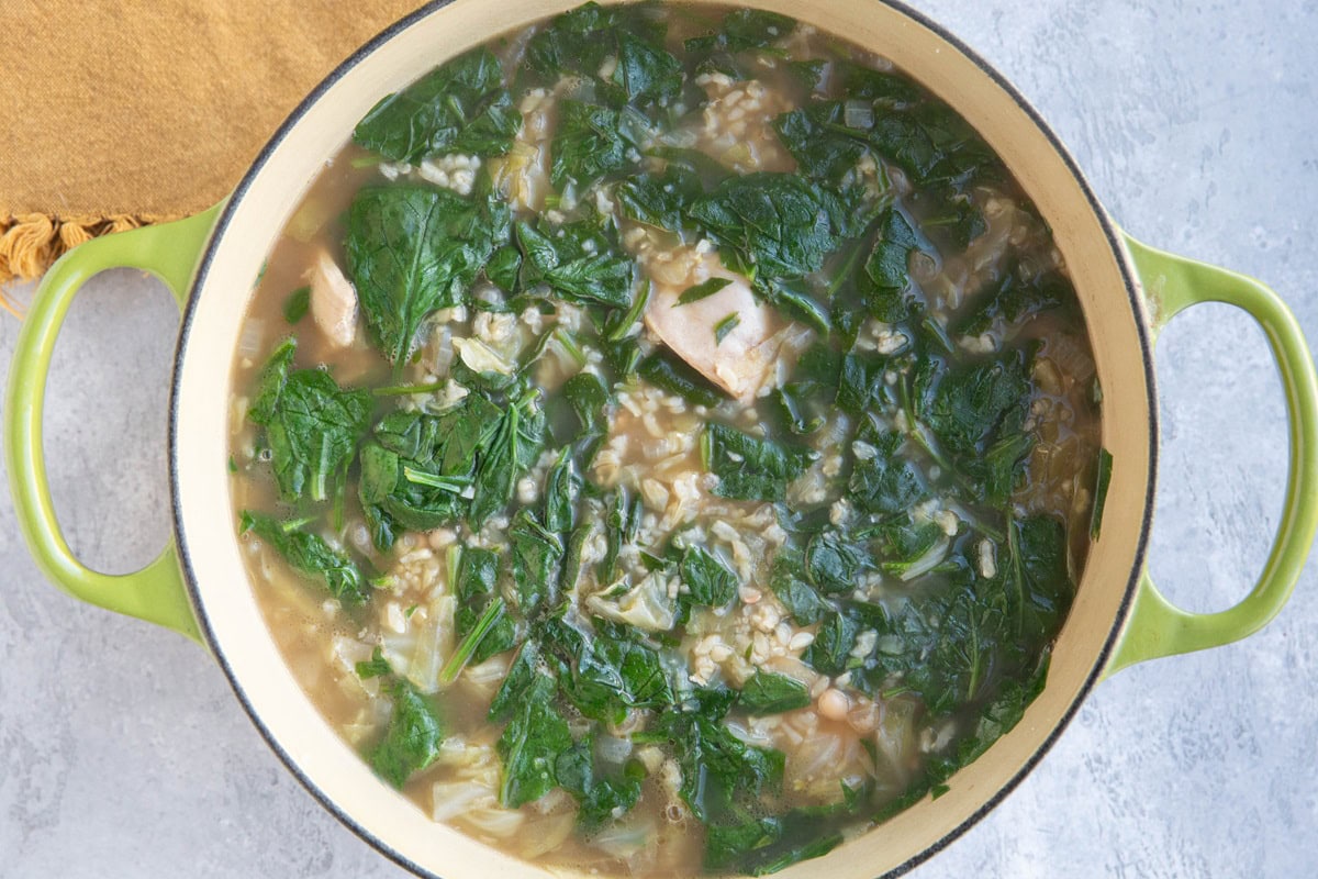 Full pot of soup with spinach, rice, cabbage, and chicken, ready to serve.