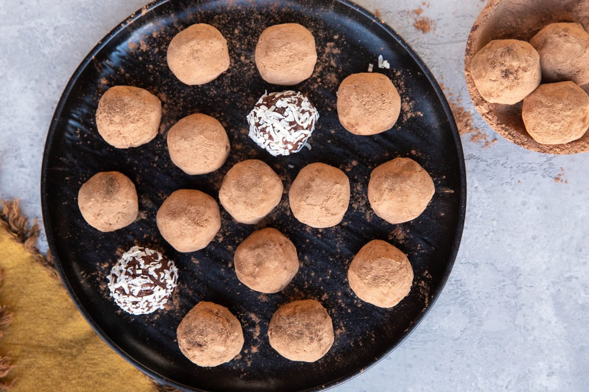 Chocolate truffles coated in cocoa powder on a black plate and three truffles in a small bowl. Ready to enjoy.