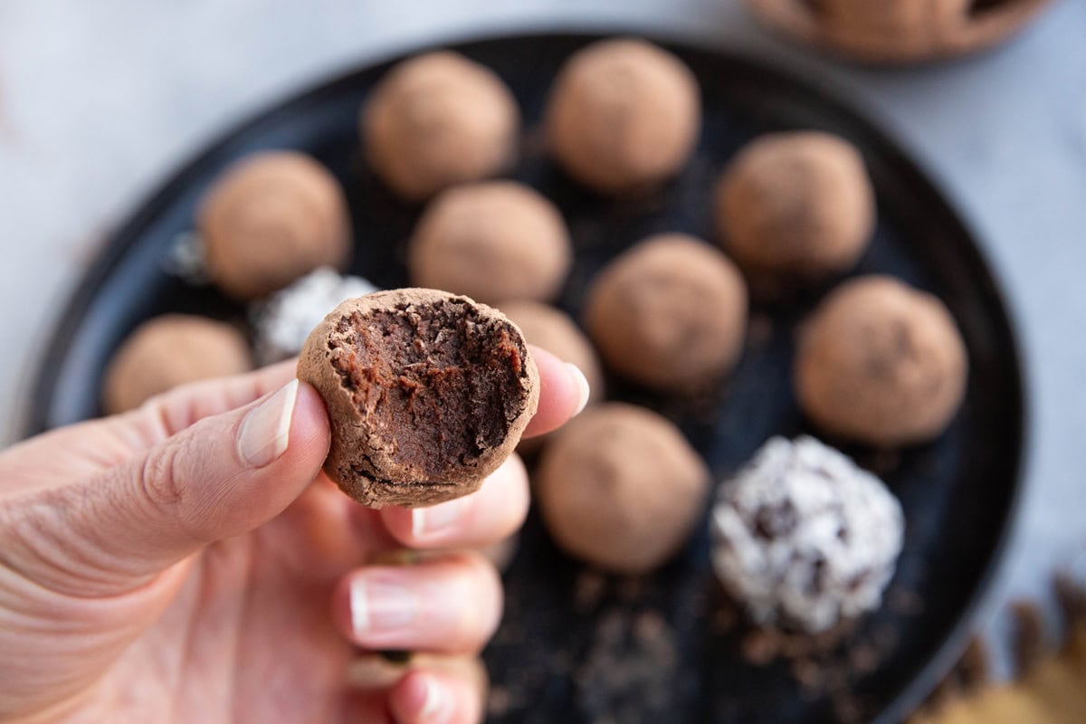 Hand holding a chickpea truffle with a bite taken out to expose the soft rich inside.