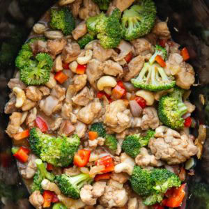 Slow cooker full of cashew chicken with fresh broccoli and bell peppers, ready to eat.