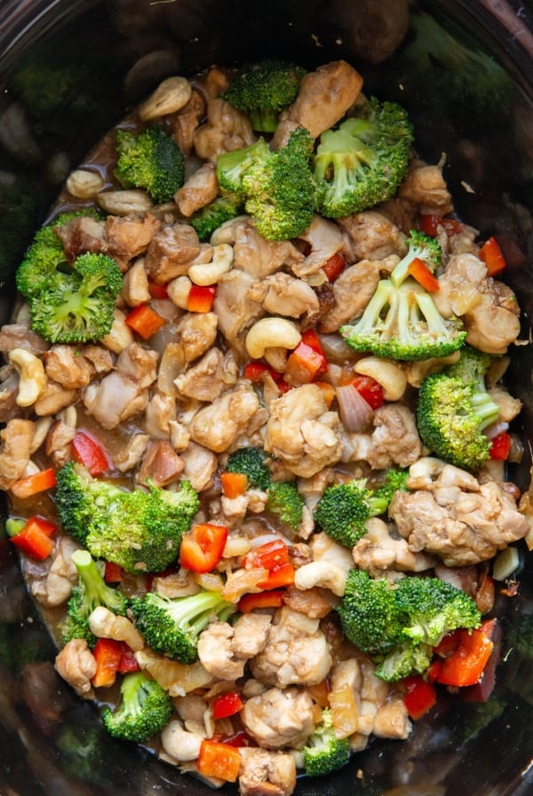 Slow cooker full of cashew chicken with fresh broccoli and bell peppers, ready to eat.
