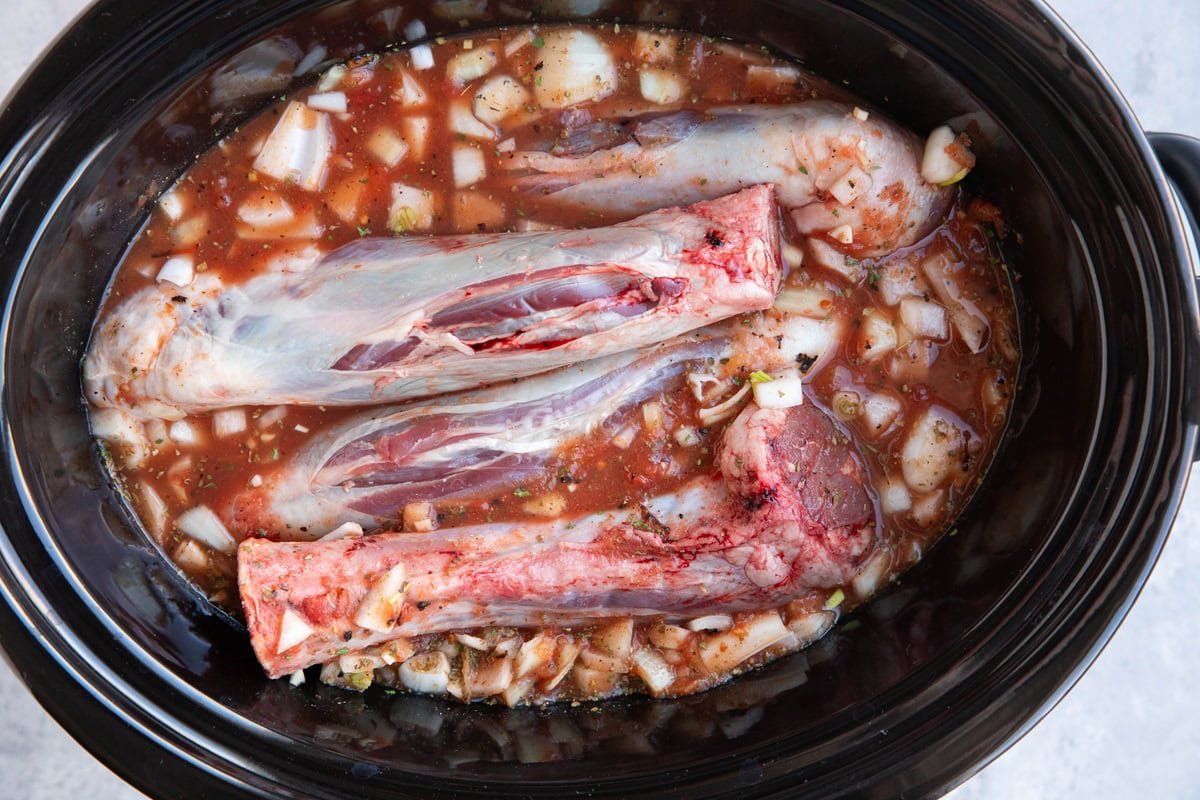 Slow cooker full of four lamb shanks in braising liquid, ready to be cooked.