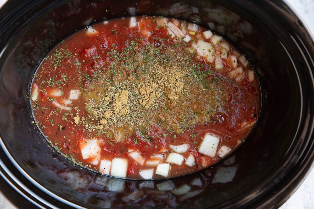 Crock pot full of onions, tomato sauce, and seasonings to serve as the braising liquid for lamb shanks.