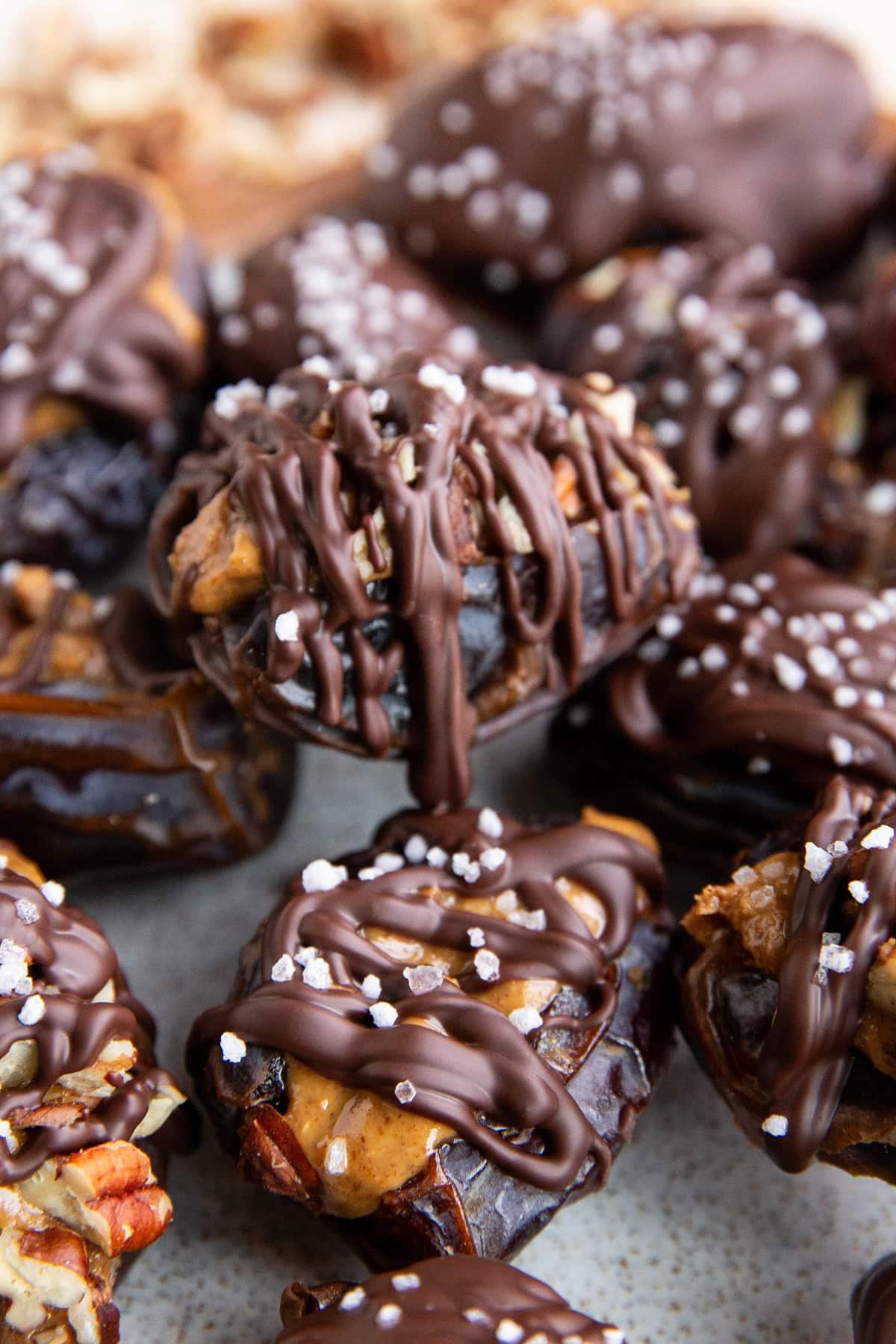 Plate of date snickers with a close up on the treats. Dates are stuffed with peanut butter and nuts then drizzled with chocolate and sprinkled with sea salt.
