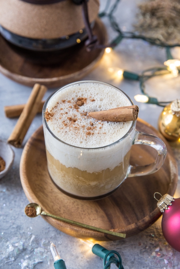 Eggnog latte in a clear coffee mug with a Chemex full of coffee in the background and Christmas lights and ornaments around.
