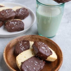 Two plates of chocolate dipped shortbread cookies with a glass of milk with a cookie on top.