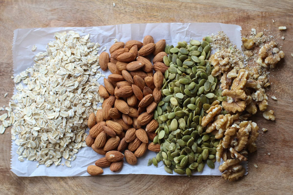 Oats, almonds, pumpkin seeds, and walnuts together on a wooden cutting board.