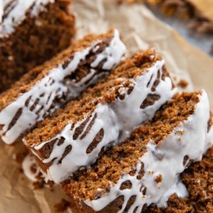 Gingerbread loaf cut into slices with glaze drizzled on top and a golden napkin in the background, ready to serve.