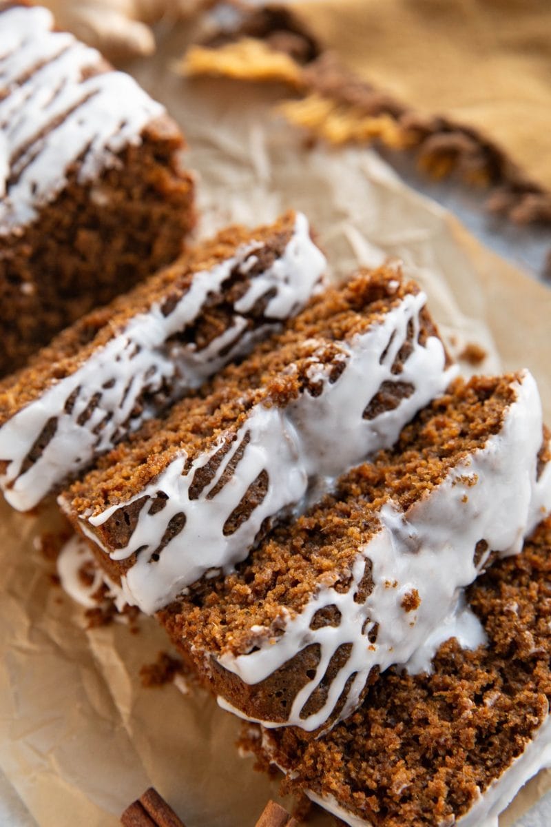 Gingerbread loaf cut into slices with glaze drizzled on top and a golden napkin in the background, ready to serve.