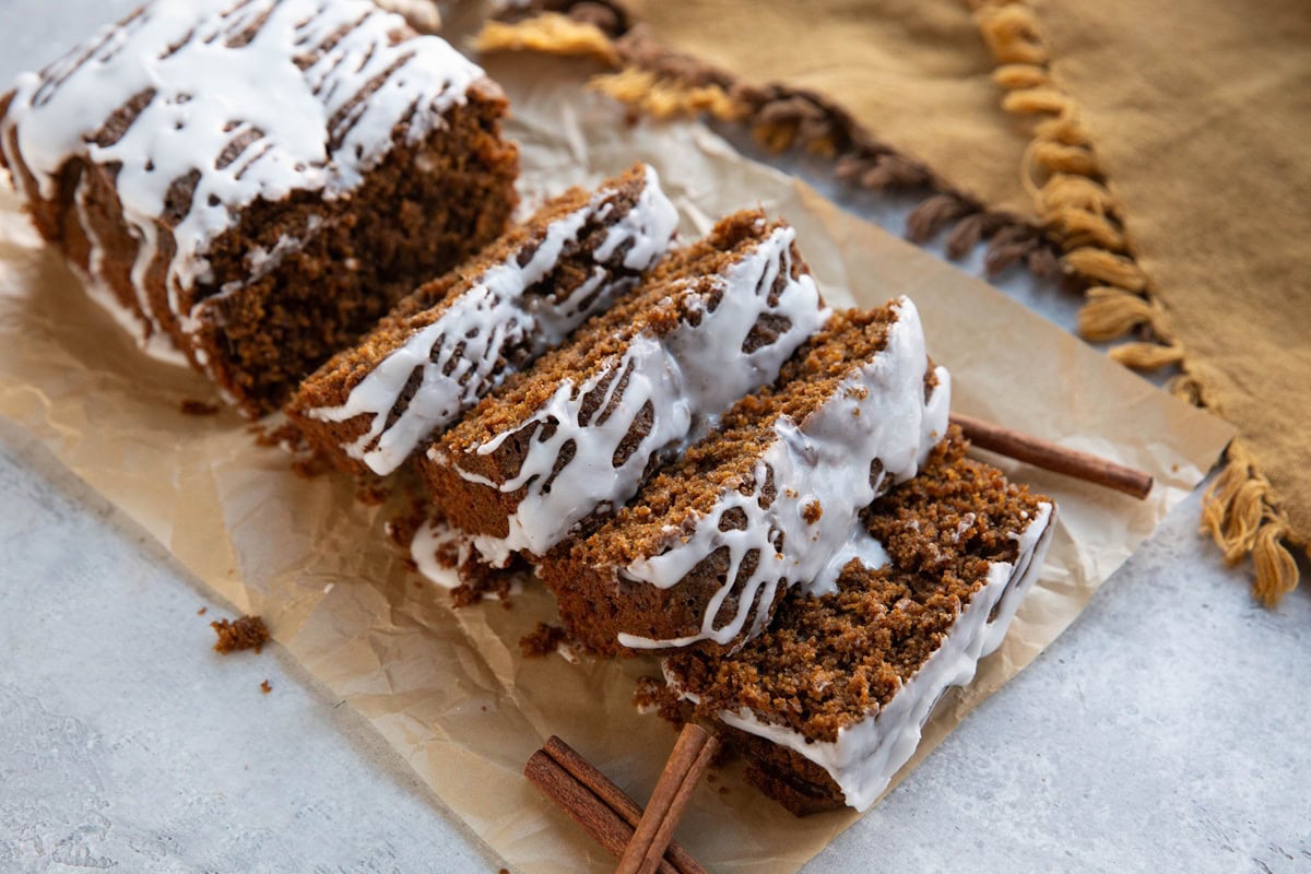 Gingerbread loaf cut into slices with a glaze drizzled on top and a golden napkin in the background.