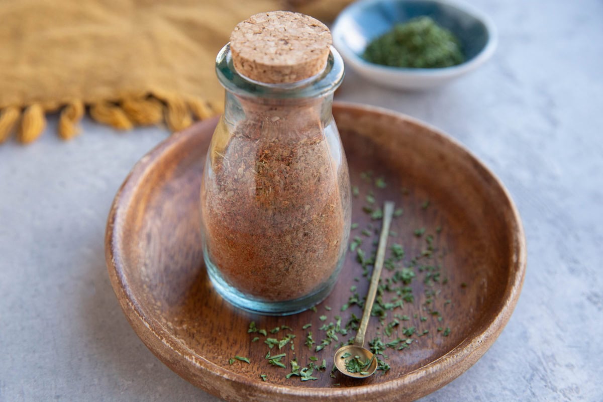 Small jar full of a homemade seasoning blend for prime rib. Dried parsley all around.