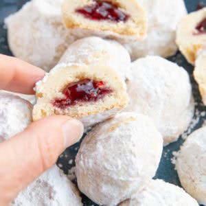 Hand picking up a raspberry snowball cookie that is cut in half, ready to eat.