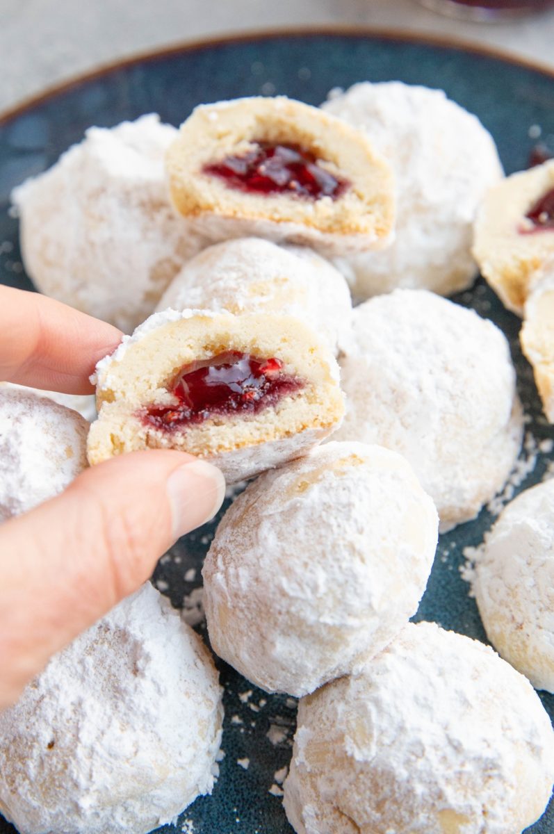Hand picking up a raspberry snowball cookie that is cut in half, ready to eat.