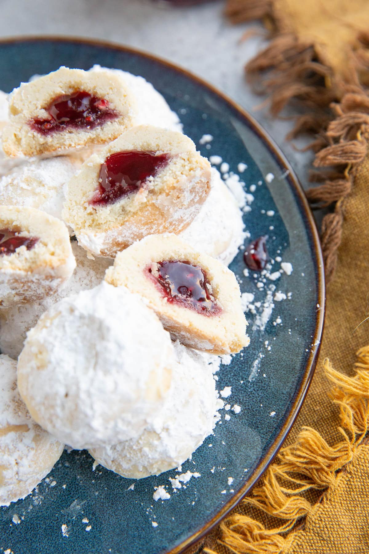 Snowball cookies stacked on a blue plate with two cut in half to expose the jammy center.