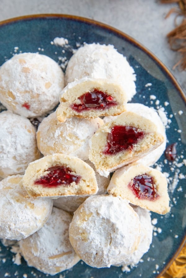 Snowball cookies on a blue plate with two cut in half, exposing the jammy center.
