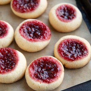 Many raspberry thumbprint cookies on a baking sheet, fresh out of the oven and ready to serve.