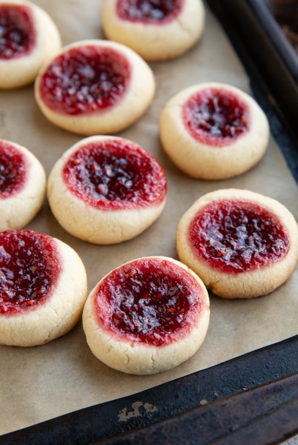 Many raspberry thumbprint cookies on a baking sheet, fresh out of the oven and ready to serve.