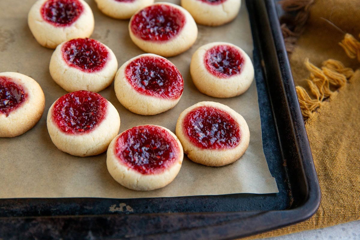Baking sheet full of raspberry thumb print cookies and a golden napkin to the side.