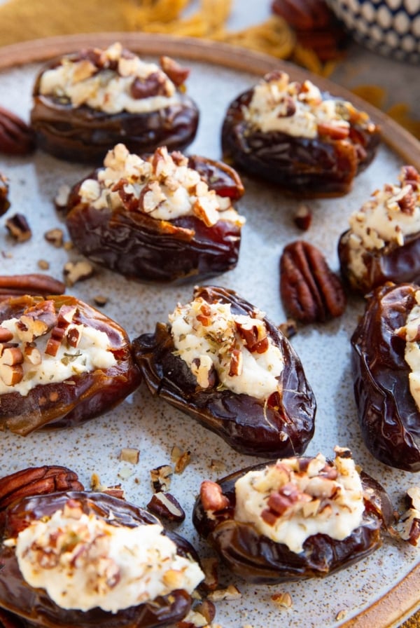 Herbed ricotta stuffed dates on a plate with chopped pecans on top, ready to serve.