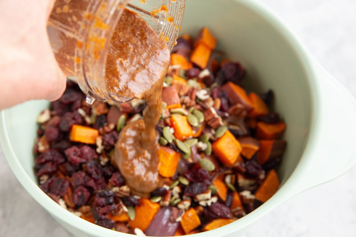 Pouring dressing into a mixing bowl with brown rice salad ingredients.