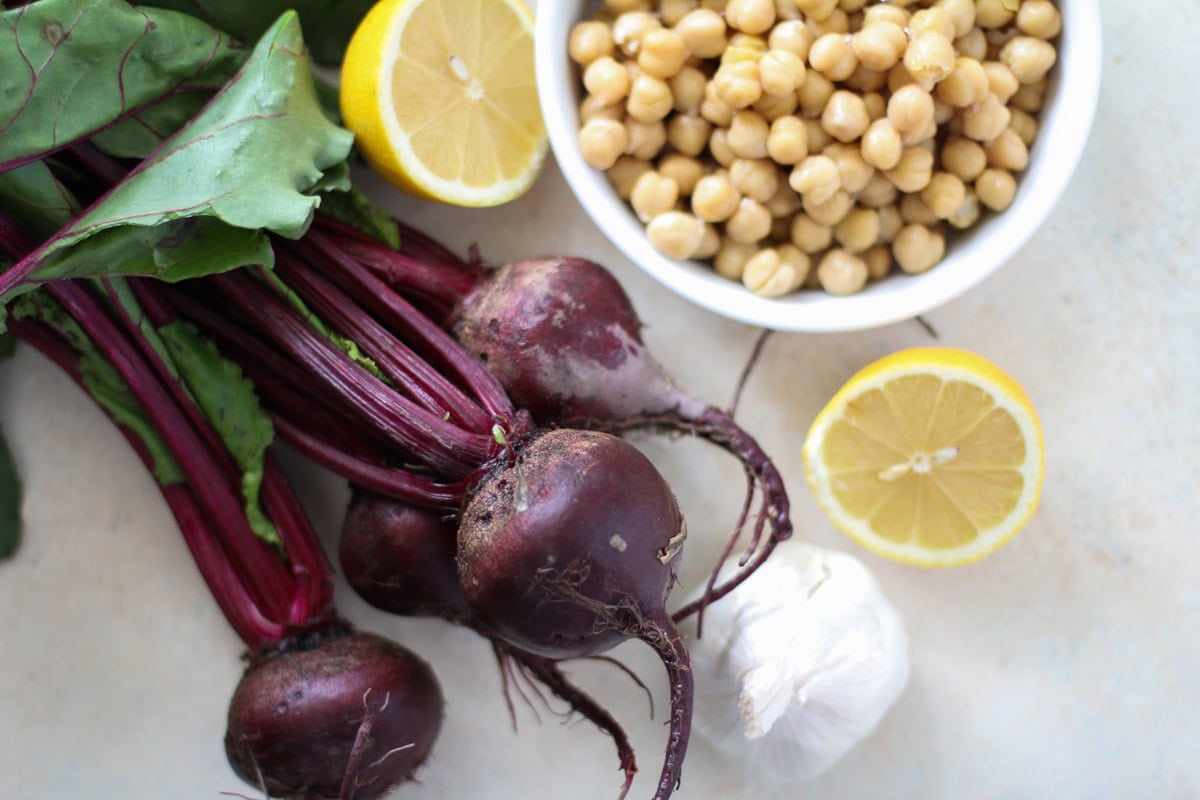 Ingredients for beet hummus on a table - lemons, garlic, garbanzo beans, and fresh beets.