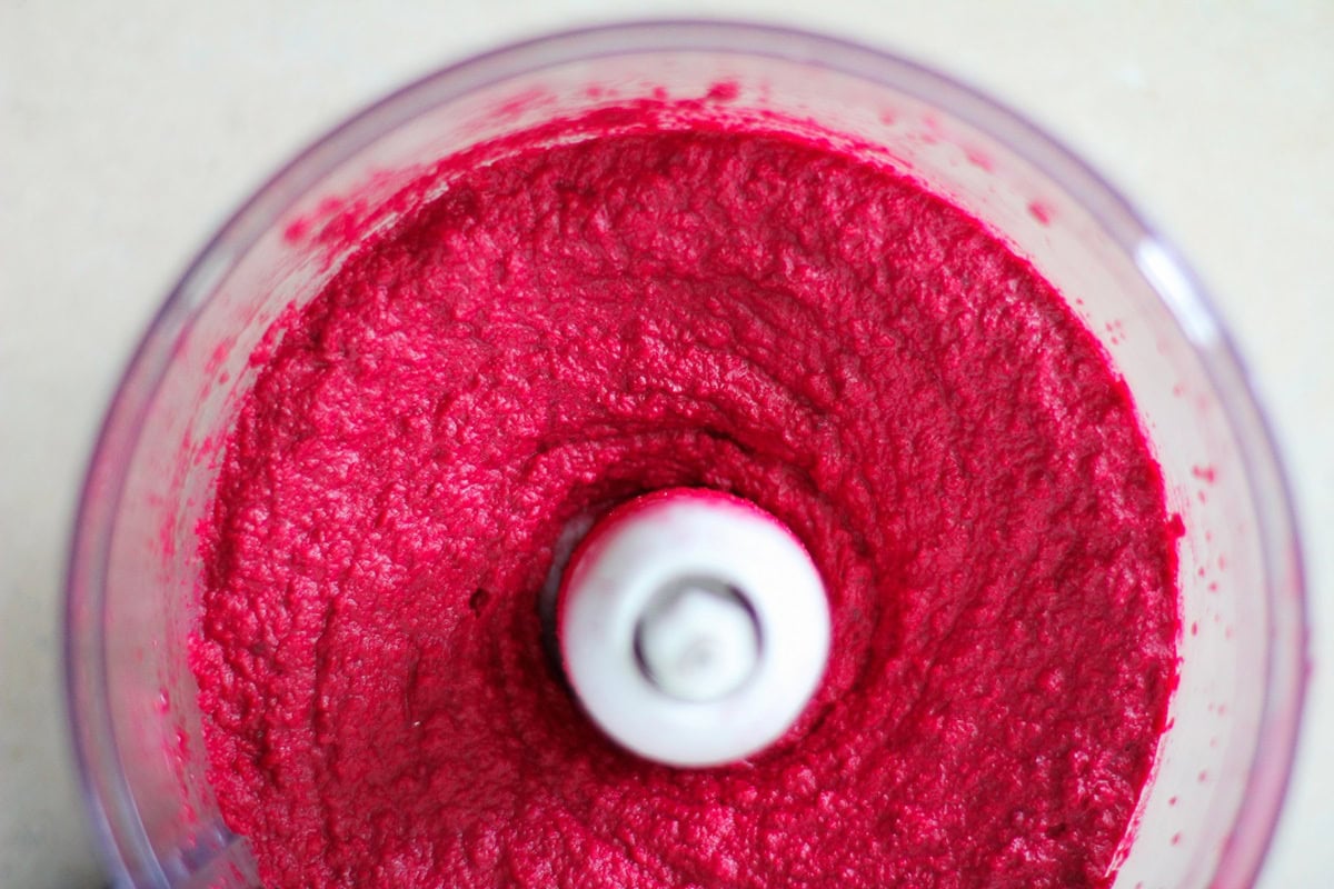 Food processor with pink hummus inside, ready to serve.