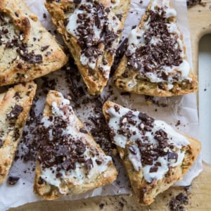 Wooden cutting board with six chocolate chip scones on top covered with glaze and more chopped dark chocolate. Ready to serve.