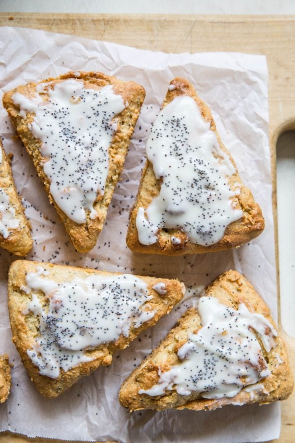 6 scones on a wooden cutting board sitting on top of parchment paper with a glaze and poppy seeds sprinkled on top.
