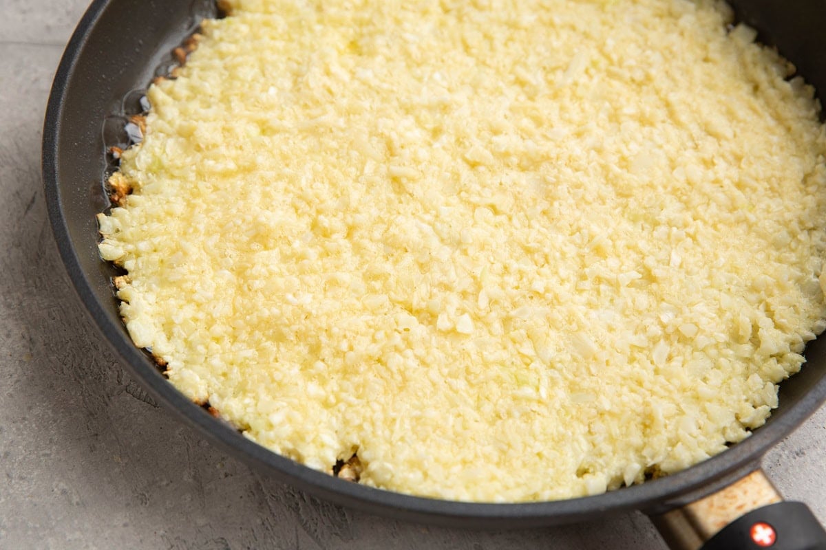 Skillet with cauliflower hash browns cooking in oil.