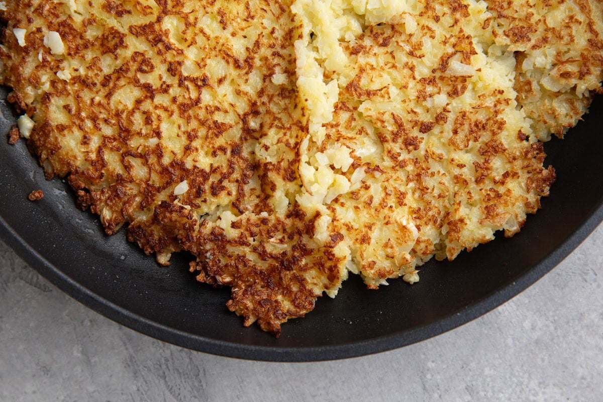Cauliflower hash browns in a skillet that are golden brown