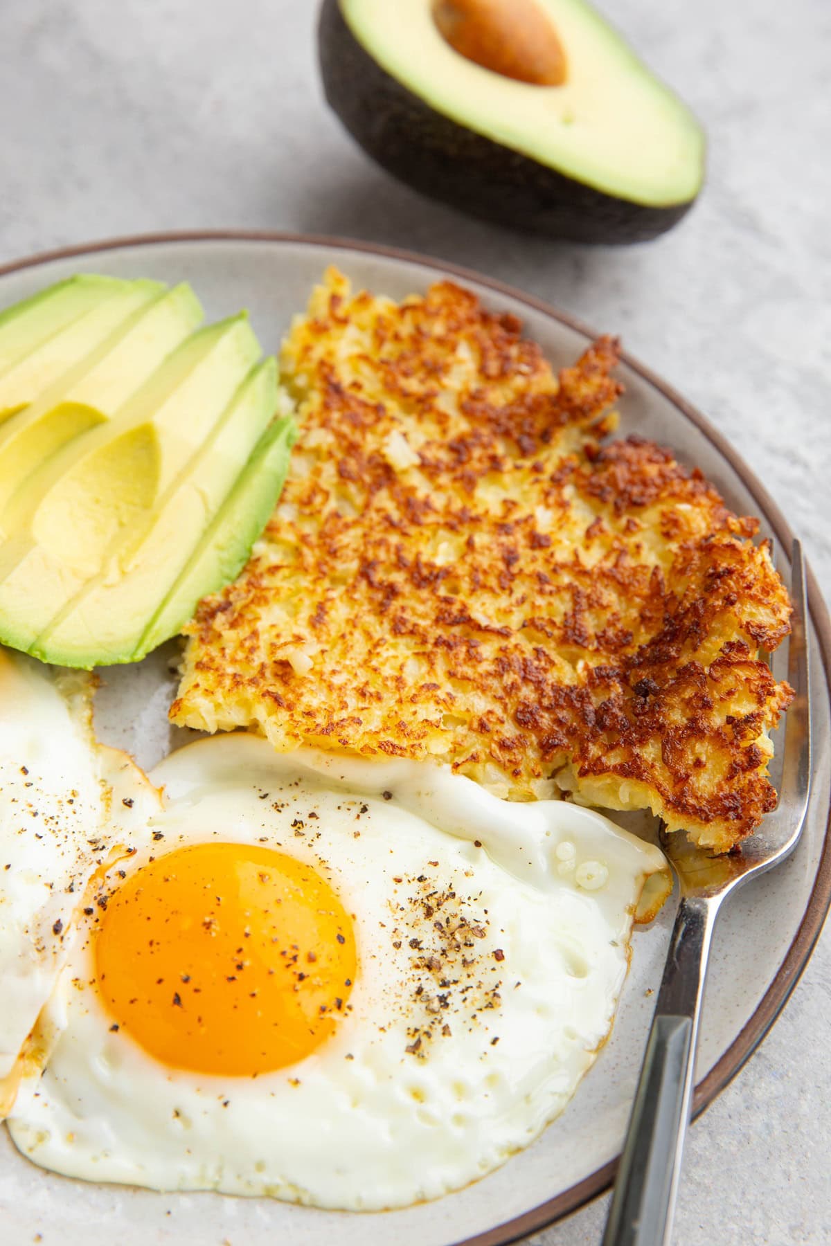 Cauliflower hash browns with sunny side up eggs and sliced avocado.