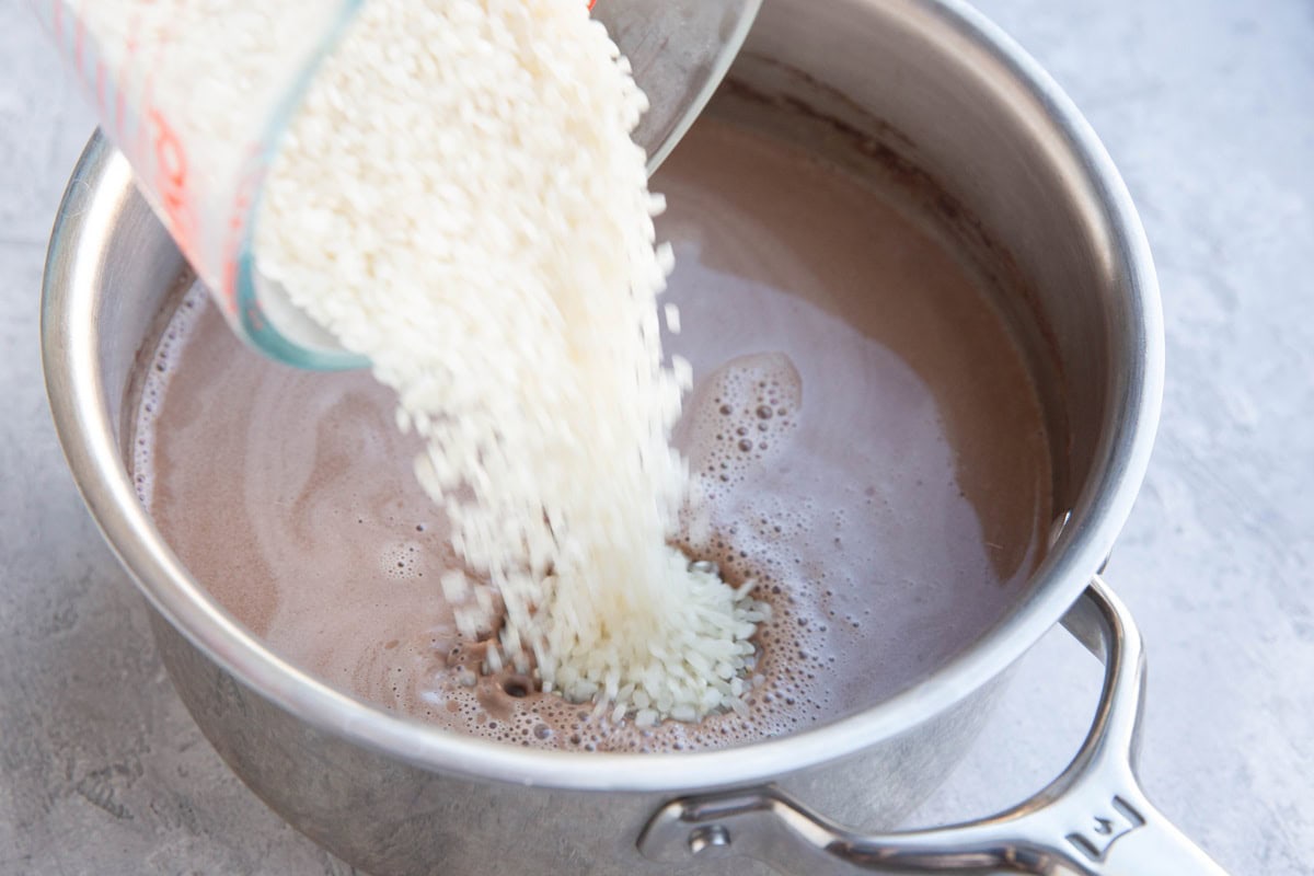 Pouring rice into a saucepan with chocolate milk.