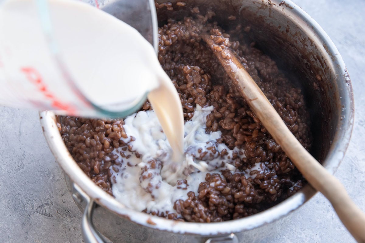 Finished chocolate rice pudding in a saucepan with milk being poured in.