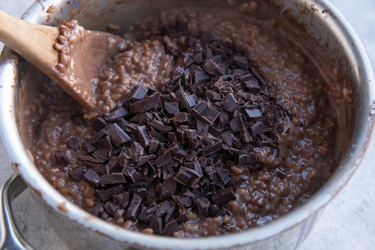 Chocolate rice pudding in a saucepan with chopped chunks of dark chocolate on top.