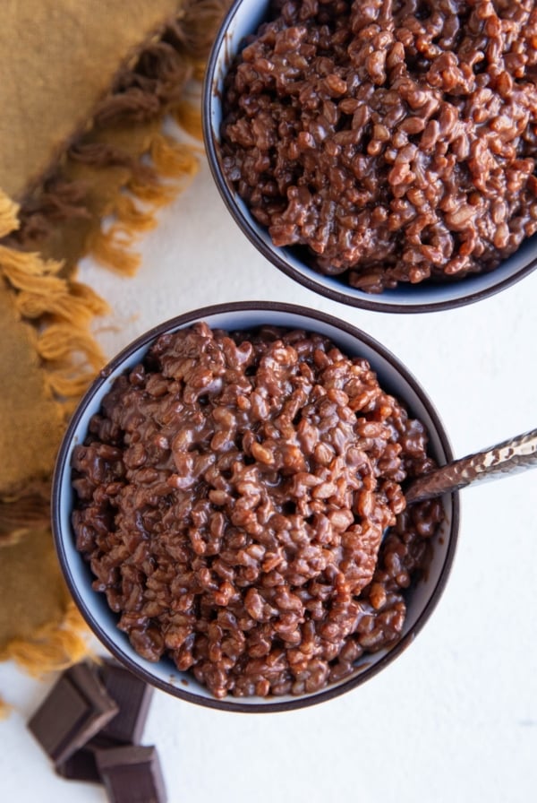 Two bowls of chocolate rice pudding with dark chocolate to the side.