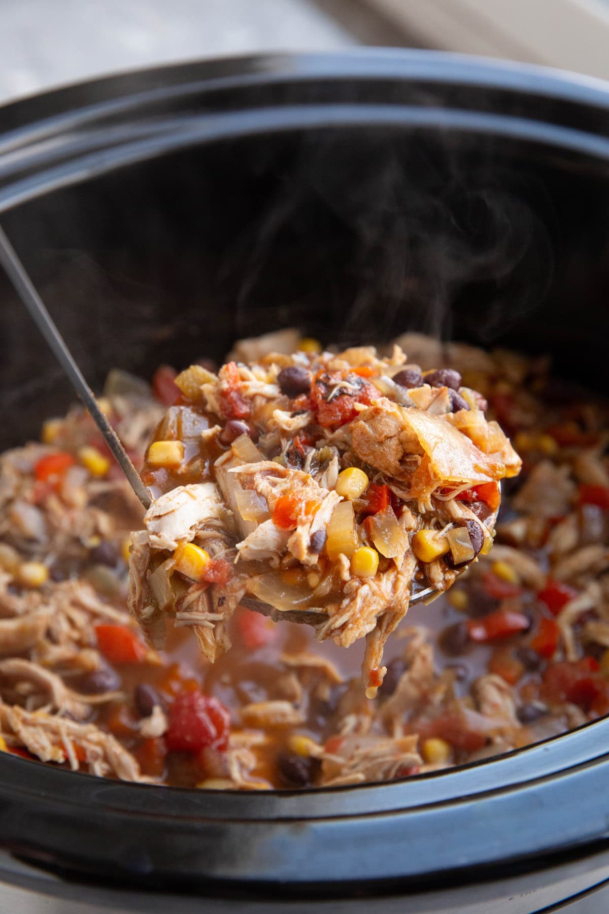 Slow cooker full of chicken chili with a ladle scooping some of the chili out to serve.