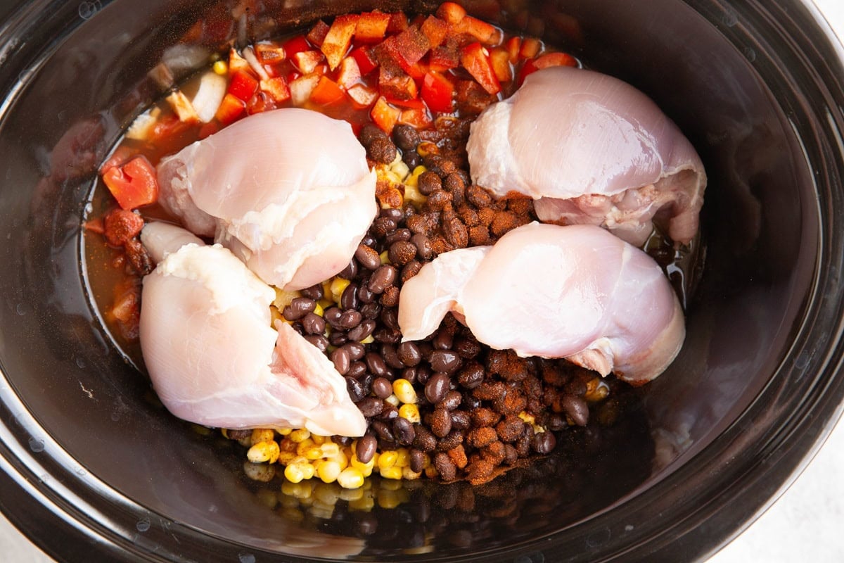 Raw chicken thighs on top of chopped bell pepper, beans, corn, chili powder and broth to make chicken chili.