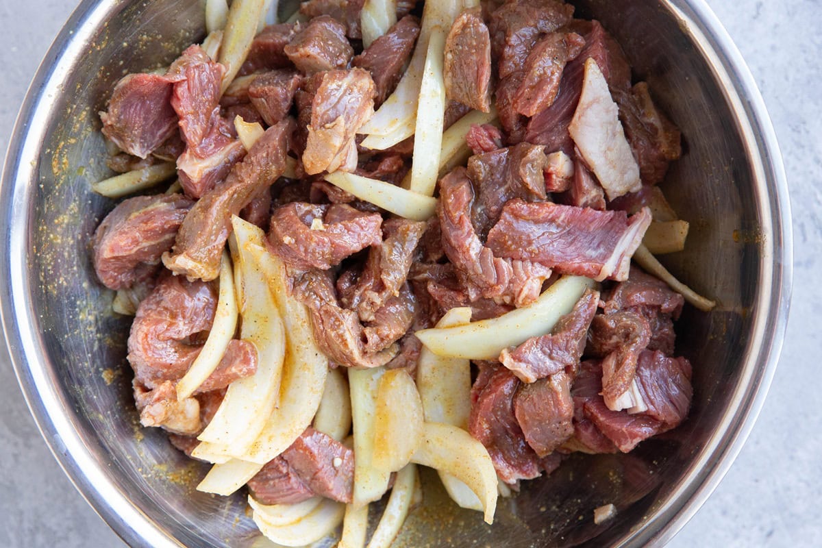 Stainless steel bowl full of sliced beef and onion tossed in shawarma marinade.