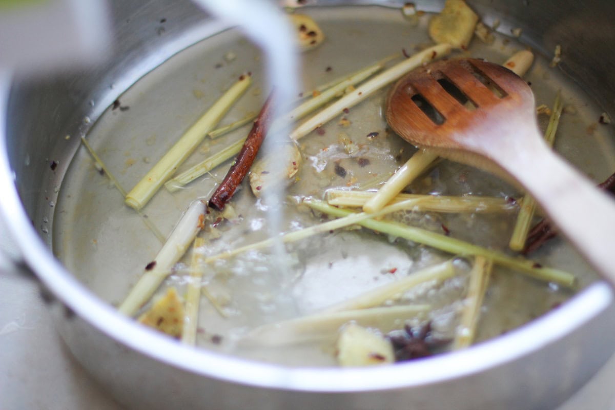 Pouring broth into the pot with the spices.