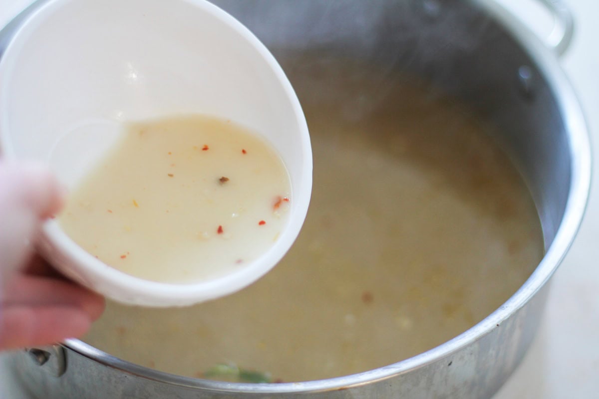 Pouring cornstarch slurry from a small bowl into the pot.