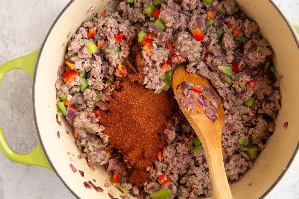 large pot full of ground meat, onion, bell peppers, and chili powder, cooking into chili.