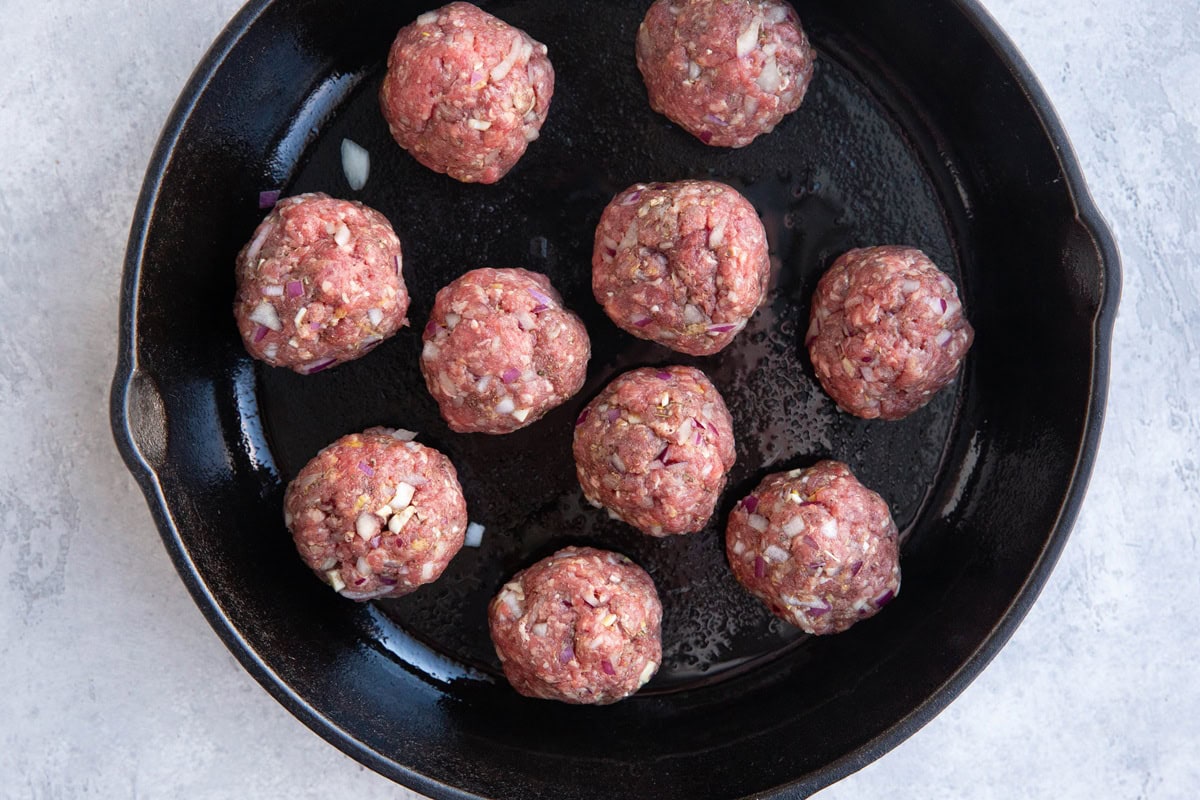 Cast iron skillet with raw meatballs inside, ready to cook