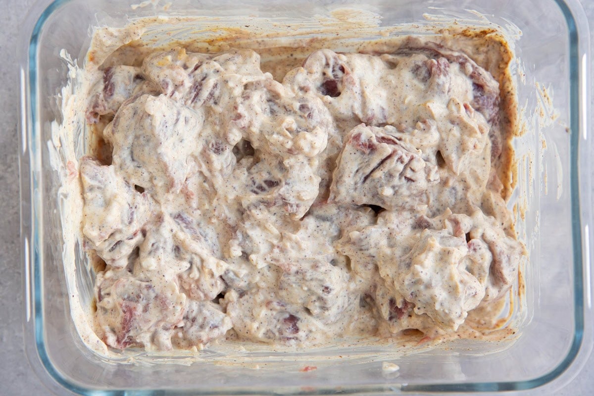 Lamb in yogurt marinade inside of a glass container to be marinated.