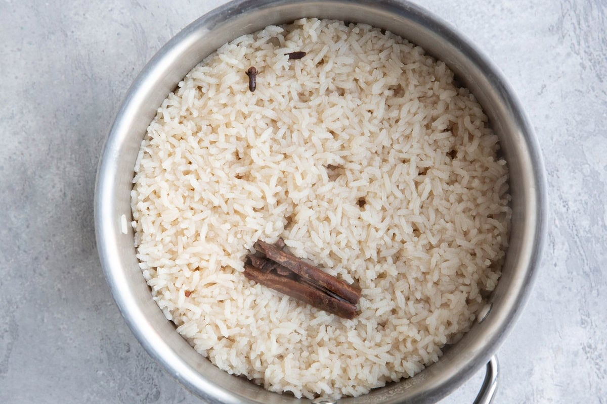 Saucepan full of cooked white rice with cinnamon stick and cloves on top.