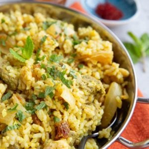 Stainless steel dish full of lamb biryani sprinkled with fresh mint. Ready to serve.